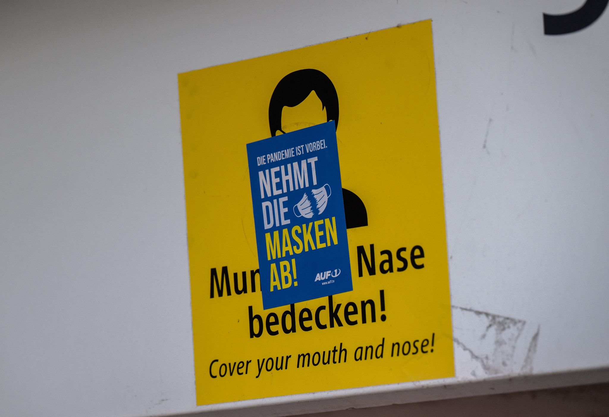 Ein Aufkleber mit der Aufschrift «Nehmt die Masken ab!» klebt über einem Schild, das zum Tragen einer Mund-Nasen-Maske auffordert. Die Mehrheit der Deutschen ist einer neuen Umfrage zufolge weiter für eine Isolationspflicht für Corona-Infizierte.