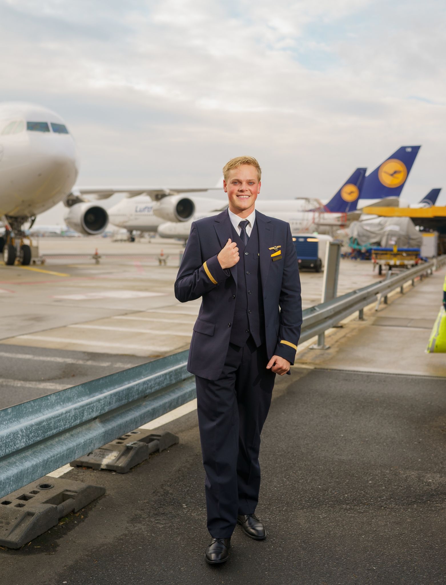 Alexander Böhmer, Lufthansa-Flugbegleiter, steht mit Dienstuniform vor mehreren Maschinen seiner Fluggesellschaft.