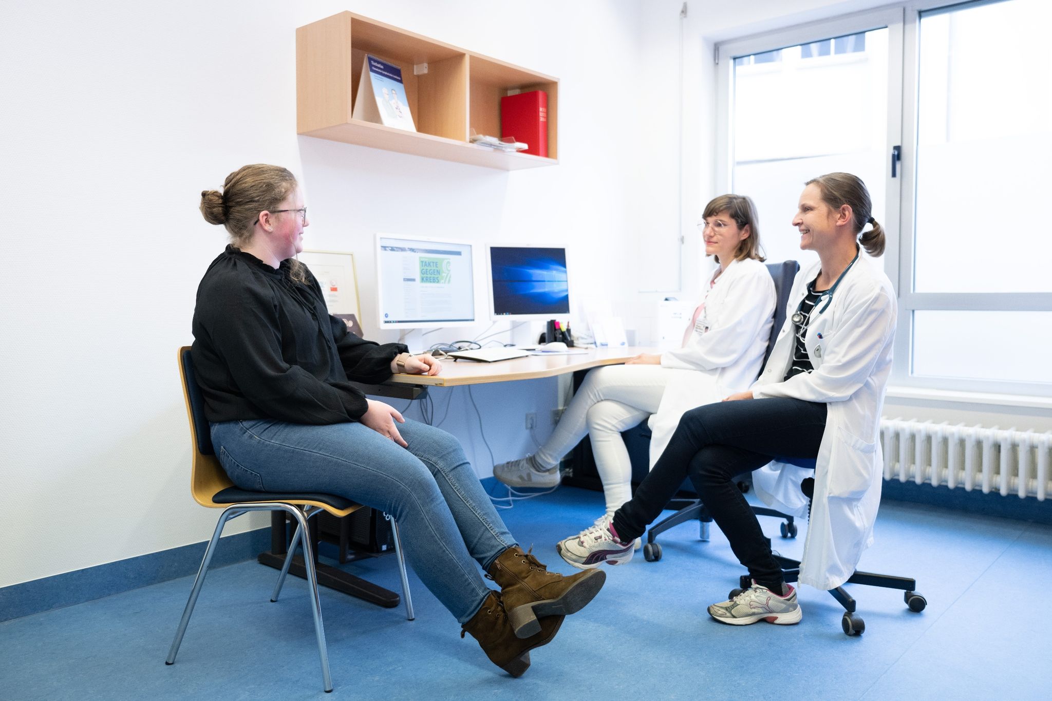 Judith Lohse (r), Kinderärztin, und Katharina Egger-Heidrich, Fachärztin Onkologie, sitzen mit einer Patientin im Nationalen Centrum für Tumorerkrankungen in einem Behandlungsraum.