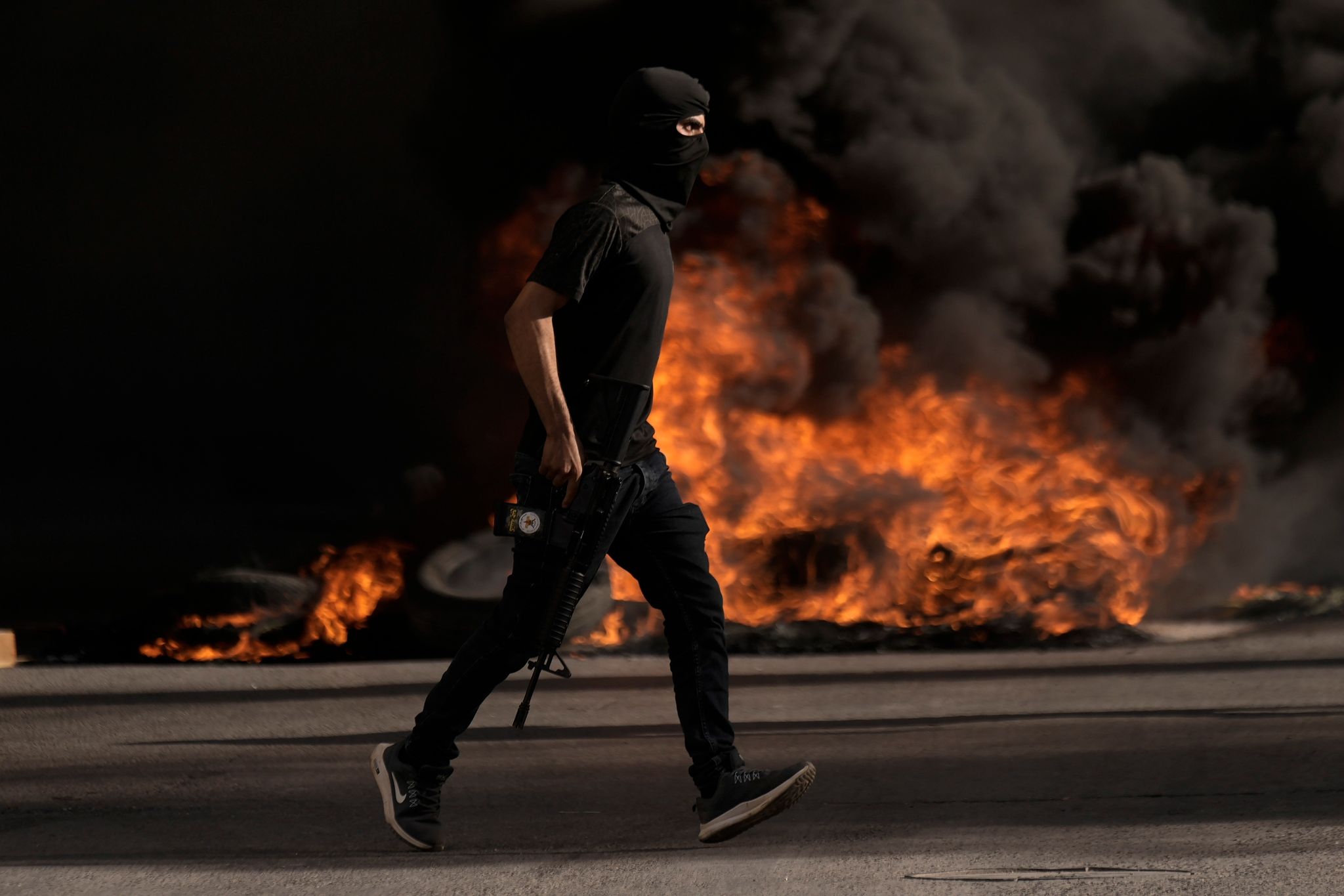 Ein bewaffnetes Mitglied der palästinensischen Sicherheitskräfte rennt bei Zusammenstößen mit israelischen Truppen vor brenneden Autoreifen entlang. Bei einem israelischen Militäreinsatz in Dschenin im Westjordanland sind mehrere Menschen getötet worden.