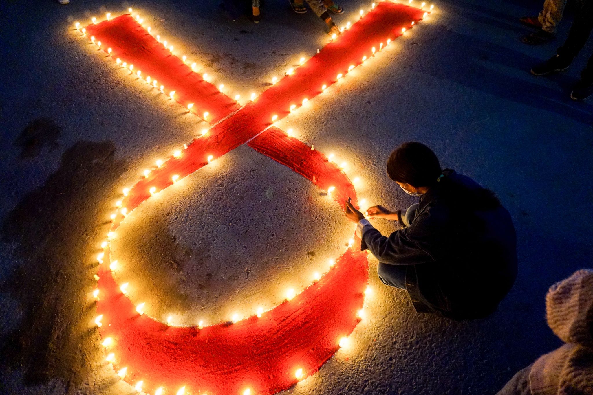 Eine Frau stellt Kerzen auf, die eine rote Schleife formen - ein weltweit anerkanntes Symbol für die Solidarität mit HIV-Infizierten.