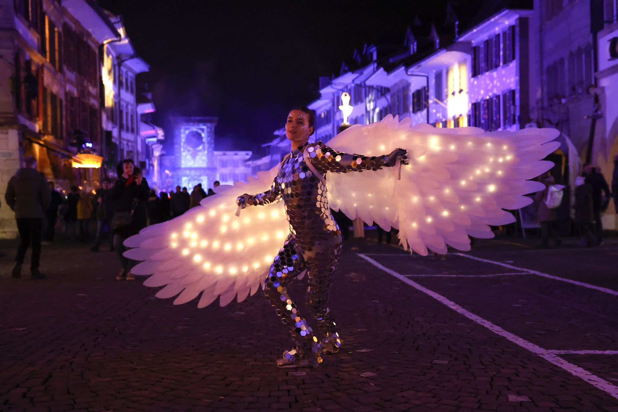Mit einer weiten Flügelspannweite ist eine Tänzerin im Disco-Outfit beim Licht-Festival im schweizerischen Murten ausgestattet.