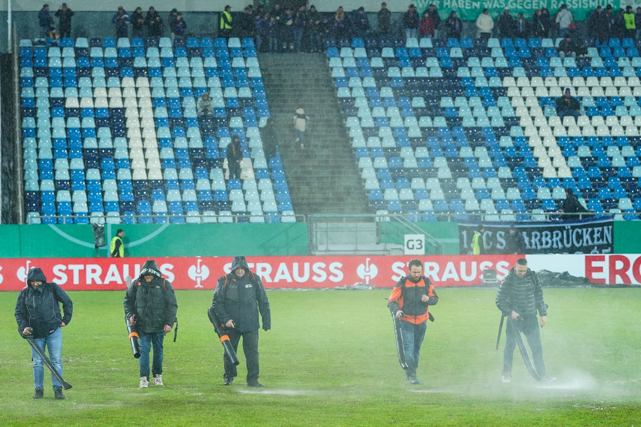 Mit Laubbläsern versuchen Helfer vor dem geplanten Anpfiff des DFB-Pokal-Viertelfinales zwischen dem 1. FC Saarbrücken und Borussia Mönchen Gladbach den Rasen von Wasser zu befreien.